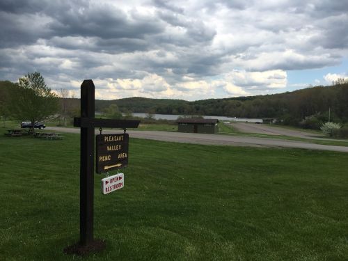 A sign for Pleasant Valley Picnic Area with a lake and cloudy sky in the background, surrounded by green grass.