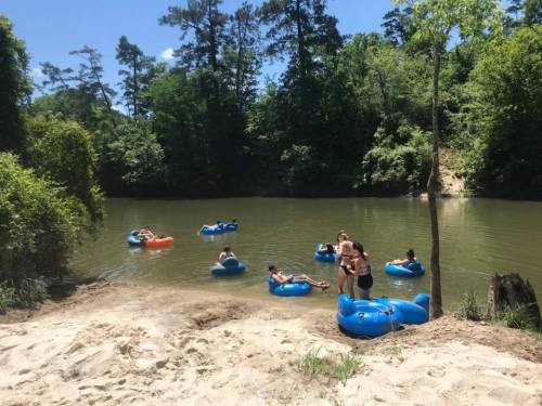People floating on blue inner tubes in a calm river surrounded by trees on a sunny day.