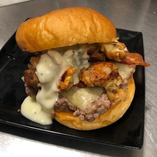 A juicy burger with melted cheese, crispy bacon, and savory toppings, served on a toasted bun on a black plate.