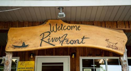 Wooden sign reading "Welcome Riverfront" with a canoe and a dog illustration.