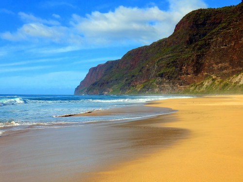 A serene beach with golden sand, gentle waves, and lush cliffs under a blue sky with scattered clouds.