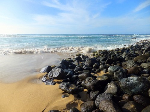 A serene beach scene with smooth rocks, gentle waves, and a clear blue sky.