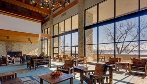 A spacious, modern lounge with large windows, wooden beams, and comfortable seating, overlooking a scenic view.