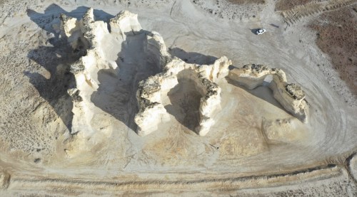 Aerial view of unique rock formations in a barren landscape, with a small vehicle nearby for scale.