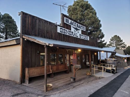 A rustic general store with wooden exterior and benches, surrounded by trees at dusk.