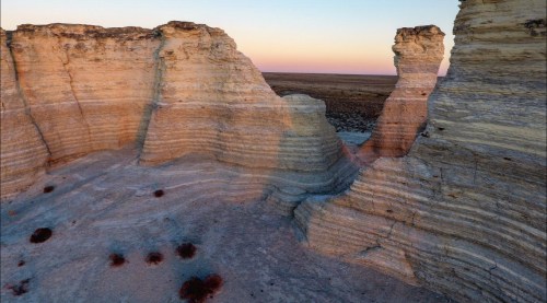 Aerial view of layered rock formations in a vast, arid landscape during sunset, showcasing natural textures and colors.