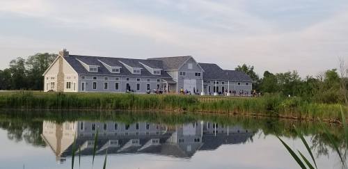 A large, modern building by a calm pond, reflecting the structure and surrounding greenery in the water.