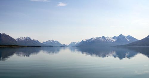 Serene lake reflecting snow-capped mountains under a clear blue sky.