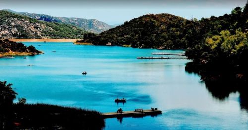 A serene lake surrounded by hills, with boats on the water and a wooden dock in the foreground.