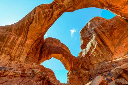 A stunning view of natural rock arches against a bright blue sky, surrounded by towering red rock formations.