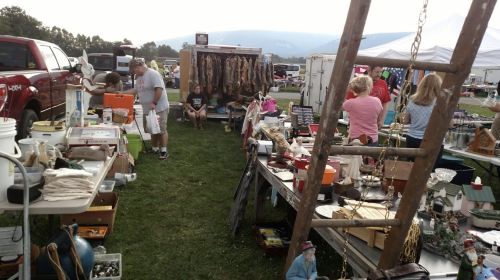 A bustling outdoor flea market with various stalls, people browsing, and items for sale on tables and displays.