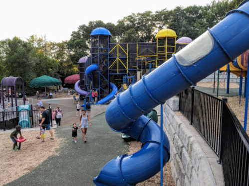 A playground with colorful slides and structures, children playing, and families enjoying the outdoor space.