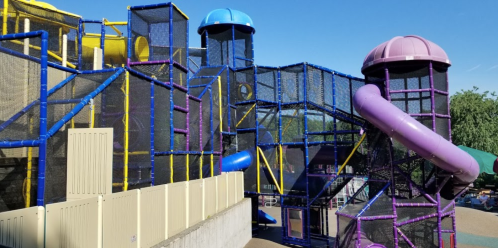 Colorful indoor play structure with slides and climbing areas, featuring blue, purple, and yellow elements against a clear sky.