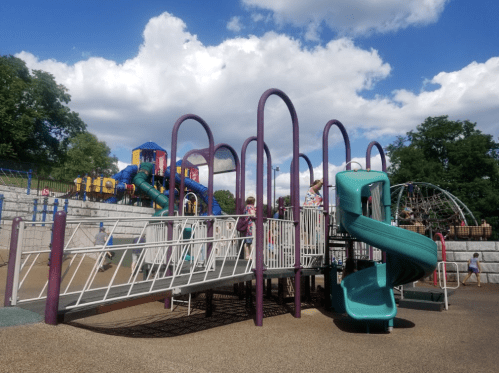 Children playing on a colorful playground with slides and climbing structures under a partly cloudy sky.