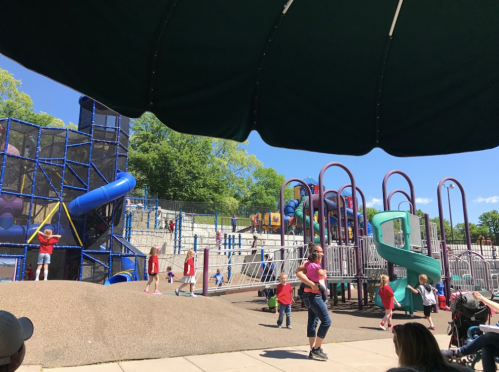 A vibrant playground with slides and climbing structures, filled with children playing under a sunny blue sky.