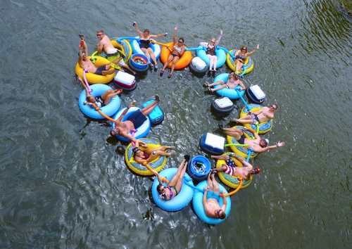 A group of people floating in inner tubes, forming a circle on a river, enjoying a sunny day.