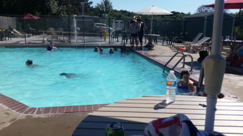 A sunny pool scene with people swimming, lounging, and socializing around the water and poolside furniture.