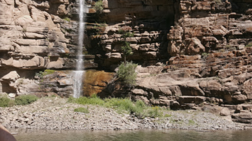 A serene waterfall cascading down rocky cliffs into a calm body of water, surrounded by lush greenery.