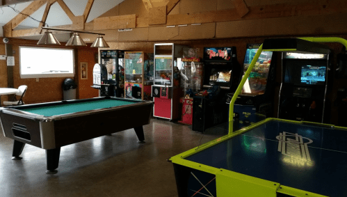 A game room featuring a pool table, arcade machines, and air hockey table in a wooden interior.