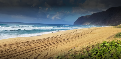 A sandy beach with gentle waves, surrounded by cliffs and a cloudy sky, creating a serene coastal scene.