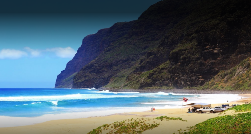 A scenic beach with waves, cliffs in the background, and a few people near parked vehicles under a clear sky.
