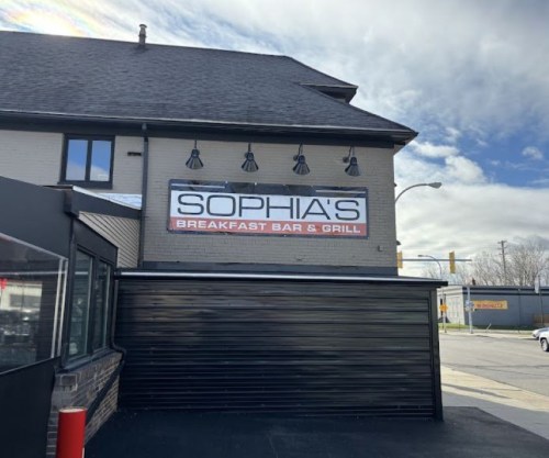 Sign for Sophia's Breakfast Bar & Grill on a building, with a cloudy sky in the background.