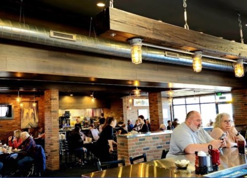 A busy restaurant interior with patrons dining and chatting, featuring brick walls and industrial lighting.