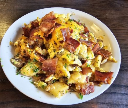 A hearty plate of scrambled eggs, crispy bacon, and diced potatoes, garnished with herbs.