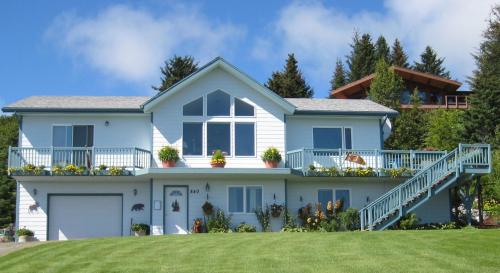 A two-story house with a blue exterior, large windows, and a green lawn, surrounded by trees and flower pots.