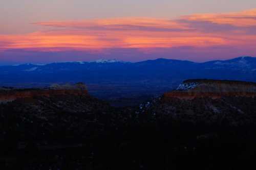 Sunset over rugged cliffs and distant mountains, with vibrant pink and purple hues in the sky.