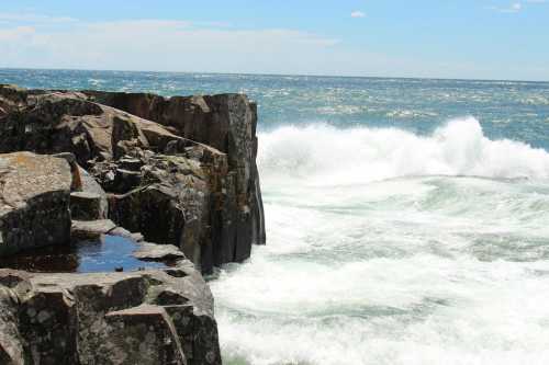 Waves crash against rocky shore under a clear blue sky, creating a dynamic coastal scene.