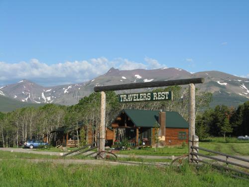 A wooden sign reading "Travelers Rest" in front of a rustic lodge, with mountains and blue sky in the background.