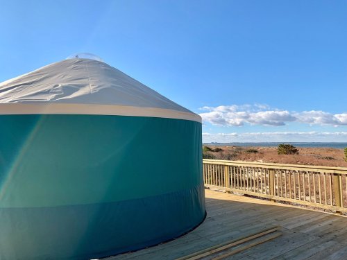 A yurt on a wooden deck overlooking a scenic landscape with blue skies and distant hills.