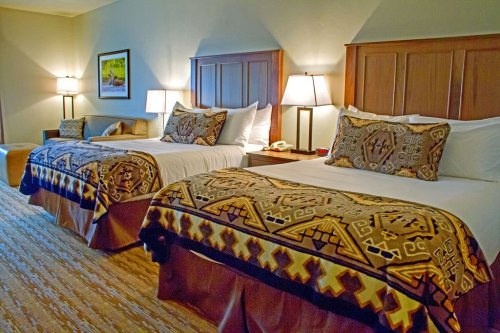 A cozy hotel room featuring two beds with patterned blankets, bedside lamps, and a warm color palette.