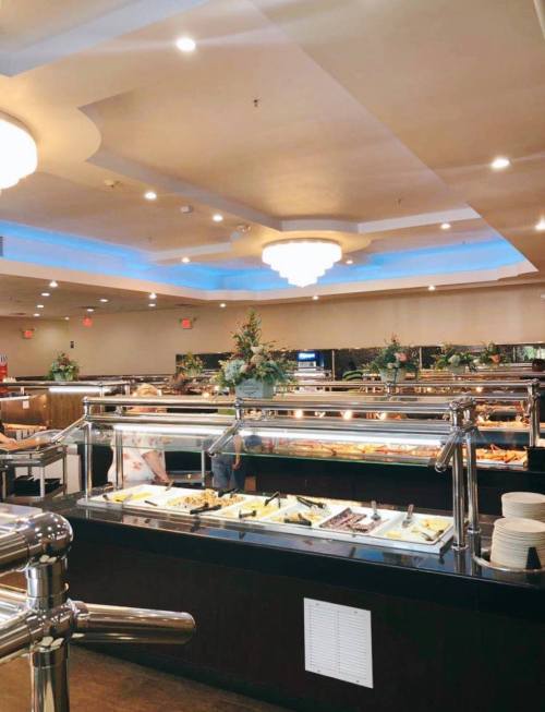 A spacious buffet restaurant with a variety of food displays and elegant decor, featuring chandeliers and floral arrangements.