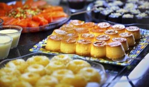 A variety of colorful desserts displayed on a table, including flan, sweets, and fruit.