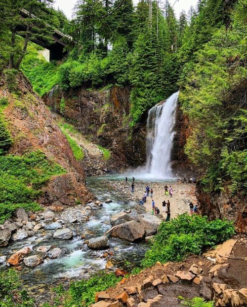 A scenic waterfall surrounded by lush greenery, with people enjoying the area near the water's edge.