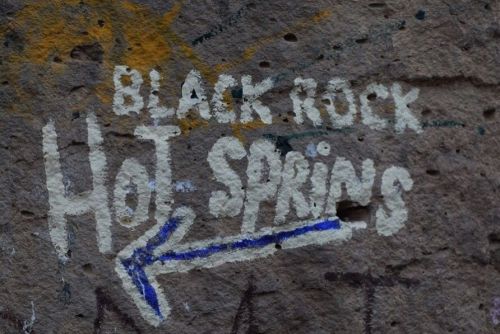 Graffiti on a rock surface indicating the direction to "Black Rock Hot Springs" with an arrow pointing left.