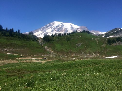 A snow-capped mountain rises above a lush green landscape under a clear blue sky.