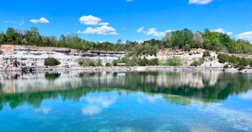 A serene quarry lake reflecting blue skies and lush greenery on the surrounding cliffs.