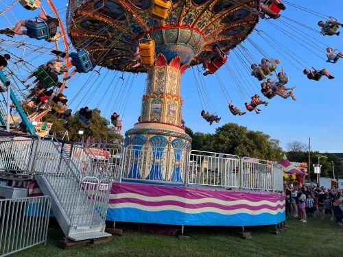 A colorful swing ride at a fair, with riders enjoying the view and a crowd gathered nearby.