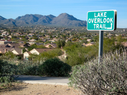 Sign for Lake Overlook Trail with mountains and a residential area in the background. Clear blue sky above.