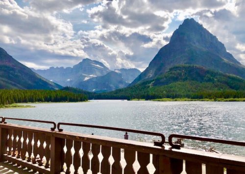 Scenic view of a lake surrounded by mountains under a cloudy sky, with a wooden railing in the foreground.