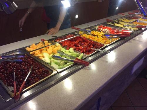 A colorful fruit bar featuring various sliced fruits in trays, including grapes, melons, strawberries, and oranges.