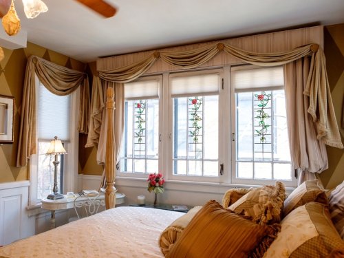 Cozy bedroom with a four-poster bed, elegant curtains, and stained glass windows, featuring soft lighting and floral decor.