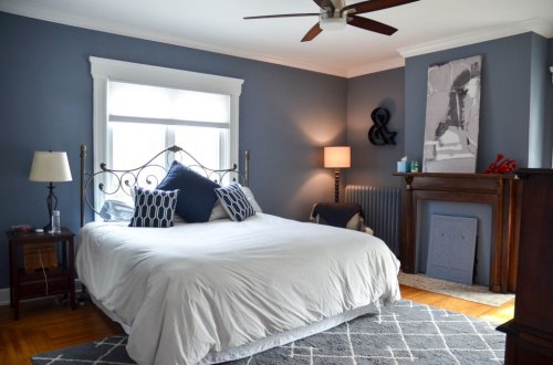 Cozy bedroom with a large bed, blue walls, a ceiling fan, and stylish decor, including a lamp and artwork.