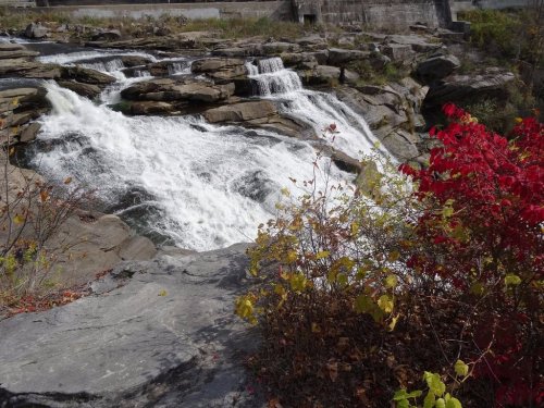 A cascading waterfall flows over rocky terrain, surrounded by colorful autumn foliage.