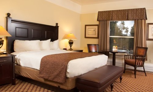 Cozy hotel room with a king bed, wooden furniture, and warm lighting, featuring a window and decorative curtains.