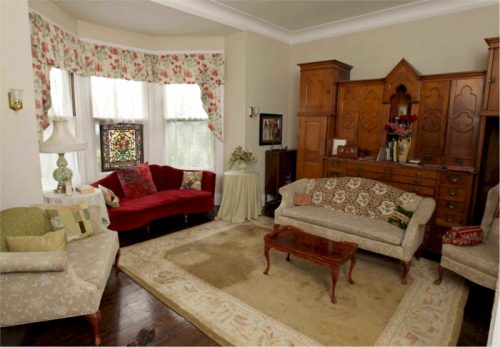 Cozy living room with floral curtains, vintage furniture, and a wooden cabinet, featuring a warm, inviting atmosphere.