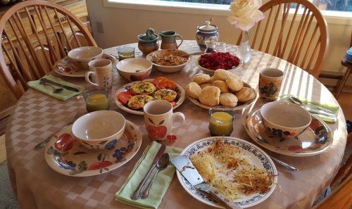 A beautifully set dining table with bowls, plates of food, drinks, and a vase of flowers, ready for a meal.